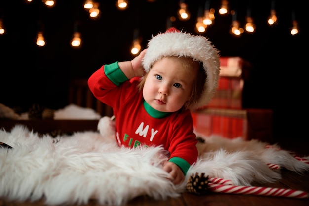 Menina bonita em uma fantasia de Natal vermelha com guirlandas retrô senta-se em uma pele