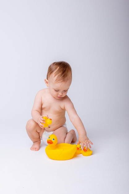 Menina bonita em uma fralda brincando com um pato de brinquedo de borracha isolado em um fundo branco