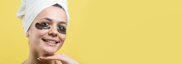 Menina bonita em uma toalha branca na cabeça usa adesivos de gel de colágeno sob os olhos Máscara sob o rosto de tratamento dos olhos