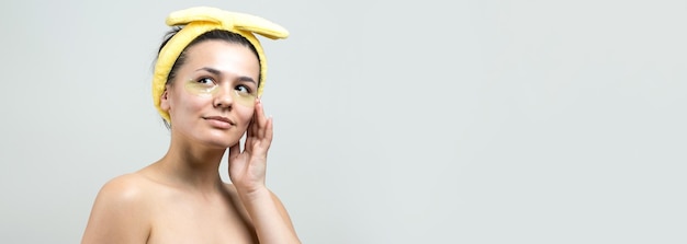 Menina bonita em uma toalha branca na cabeça usa adesivos de gel de colágeno sob os olhos Máscara sob o rosto de tratamento dos olhos