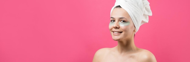 Menina bonita em uma toalha branca na cabeça usa adesivos de gel de colágeno sob os olhos máscara sob o rosto de tratamento dos olhos