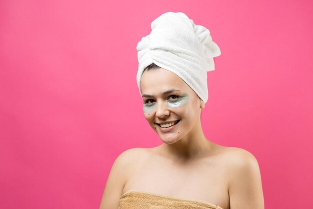 Menina bonita em uma toalha branca na cabeça usa adesivos de gel de colágeno sob os olhos