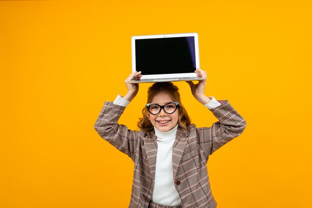 Menina bonita engraçada em uma jaqueta clássica mantém um laptop acima da cabeça