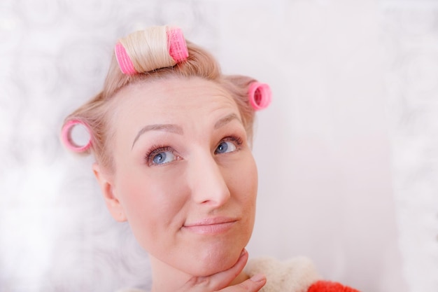 Menina bonita enrola o cabelo em rolos Jovem pensativa pensa em um penteado da moda na cabeça um grande rolo rosa
