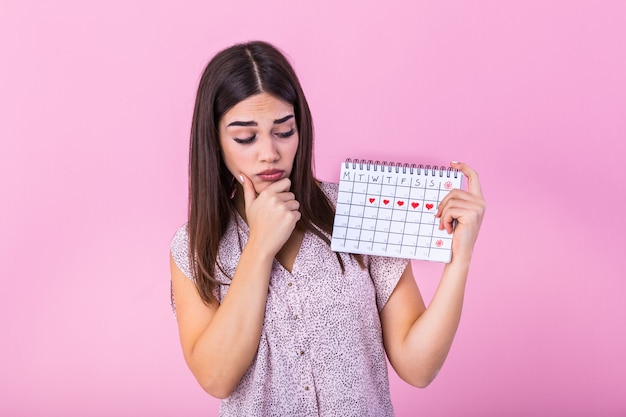 Menina bonita envergonhada, segurando o calendário menstrual