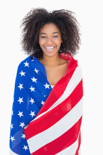 Menina bonita envolvida na bandeira americana, sorrindo para a câmera