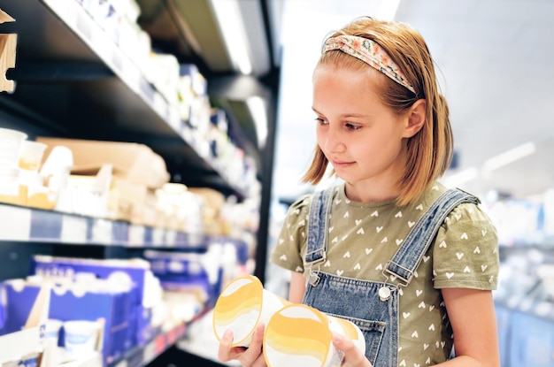 Menina bonita escolhendo iogurte na loja do supermercado bela menina pré-adolescente procurando leite