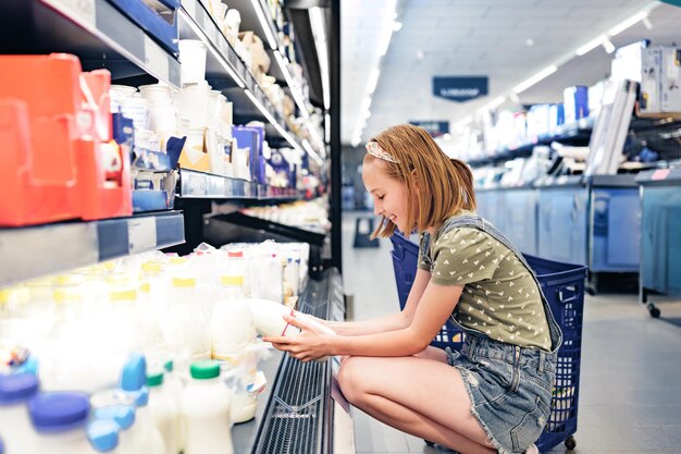 Menina bonita escolhendo leite na loja do supermercado bela menina pré-adolescente olhando lactose