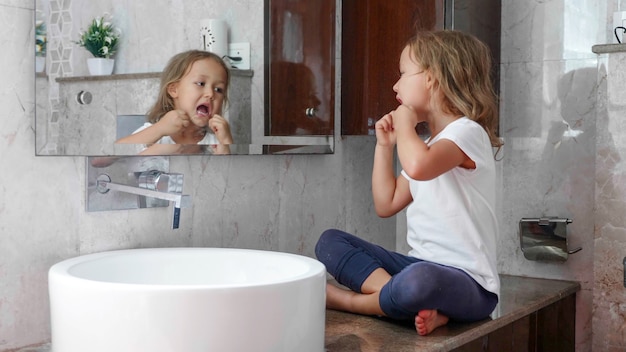 Menina bonita escova os dentes com fio dental na frente do espelho