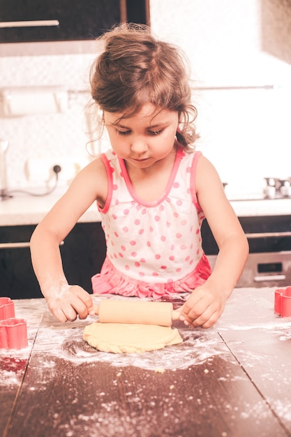 Menina bonita esticando a massa na cozinha