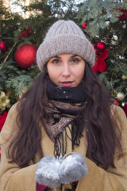 Menina bonita feliz durante as férias de Natal em luvas segurando neve