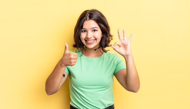 Menina bonita feliz, maravilhada, satisfeita e surpresa, mostrando gestos de ok e polegar para cima, sorrindo