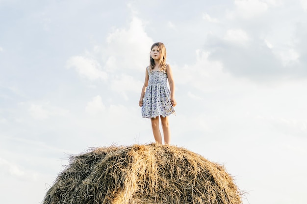 Menina bonita fica no topo do palheiro olhando para longe Lindo céu azul Liberdade Verão resto vida no campo