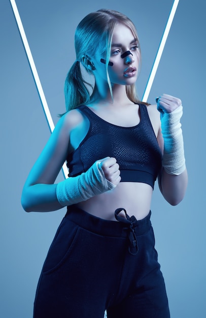 Foto menina bonita forte com cabelos loiros, olhar confiante, punhos em bandagens protetoras de boxe