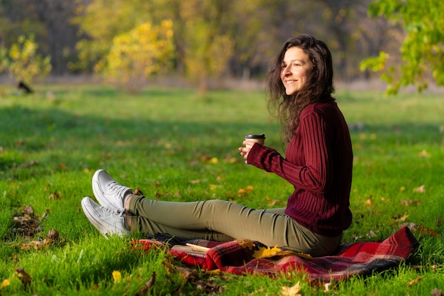 Menina bonita gosta de outono e a beleza da natureza sentada em um gramado verde no parque. Humor de outono.