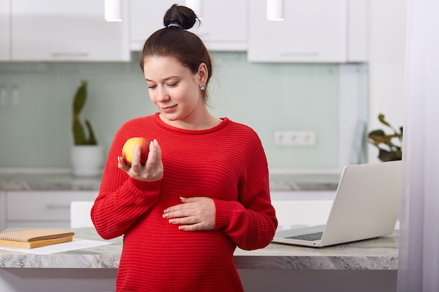 Menina bonita grávida segurando a maçã na mão.