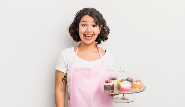 Menina bonita hispânica parecendo feliz e agradavelmente surpreso com o conceito de bolos caseiros