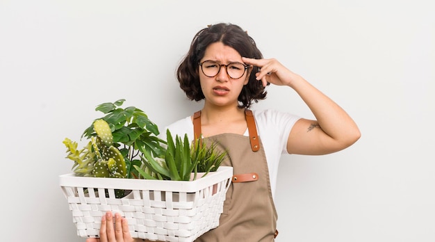 Menina bonita hispânica se sentindo confusa e intrigada mostrando que você é um conceito de plantas insanas