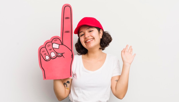 Foto menina bonita hispânica sorrindo alegremente acenando com a mão dando as boas-vindas e cumprimentando você conceito de fã número um