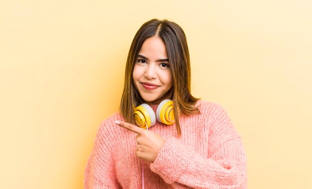 Menina bonita hispânica sorrindo alegremente se sentindo feliz e apontando para o conceito de fones de ouvido laterais