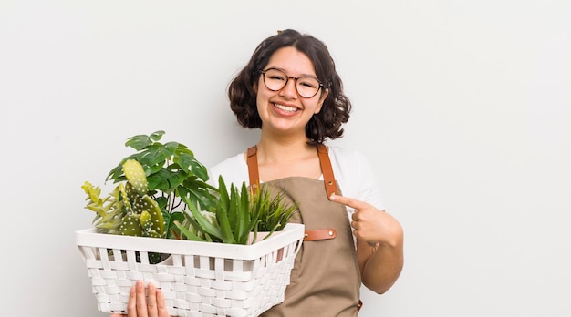 Menina bonita hispânica sorrindo alegremente se sentindo feliz e apontando para o conceito de plantas laterais