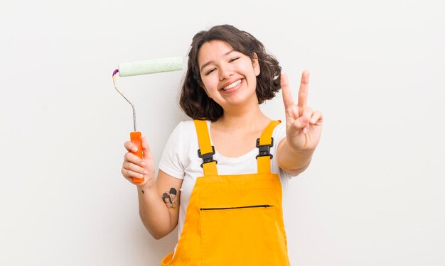 Menina bonita hispânica sorrindo e parecendo feliz gesticulando vitória ou conceito de pintura de paz em casa