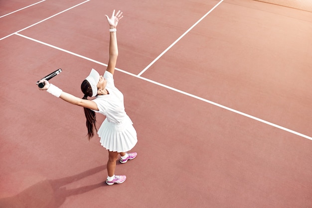 Menina bonita jogando tênis na quadra ao ar livre se preparando para bater em uma bola