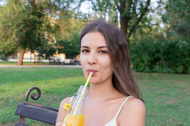 Menina bonita jovem está bebendo limonada da garrafa através da palha com um grande prazer