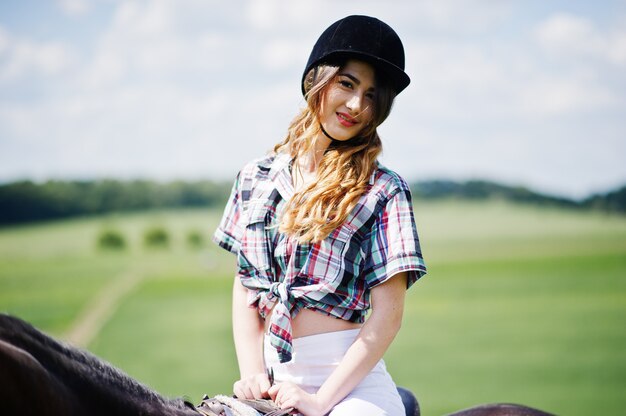 Menina bonita jovem, montando um cavalo em um campo em dia de sol.