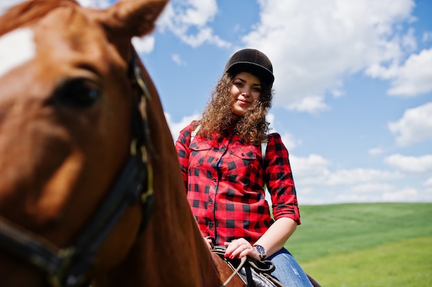 Menina bonita jovem, montando um cavalo em um campo em dia de sol.