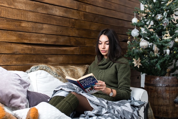 Menina bonita lendo um livro em uma atmosfera de Natal