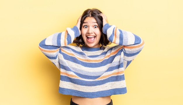 Menina bonita levando as mãos à cabeça, de boca aberta, sentindo-se extremamente sortuda, surpresa, animada e feliz