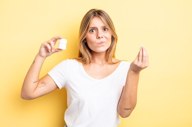 Menina bonita loira fazendo capice ou gesto de dinheiro, dizendo para você pagar. conceito de frasco de comprimidos