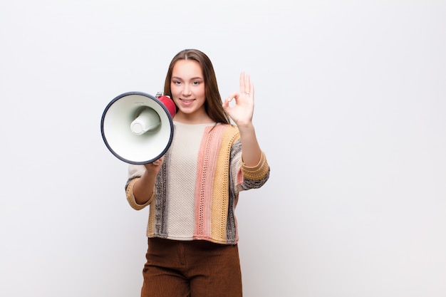 Menina bonita loira jovem com um megafone contra parede branca