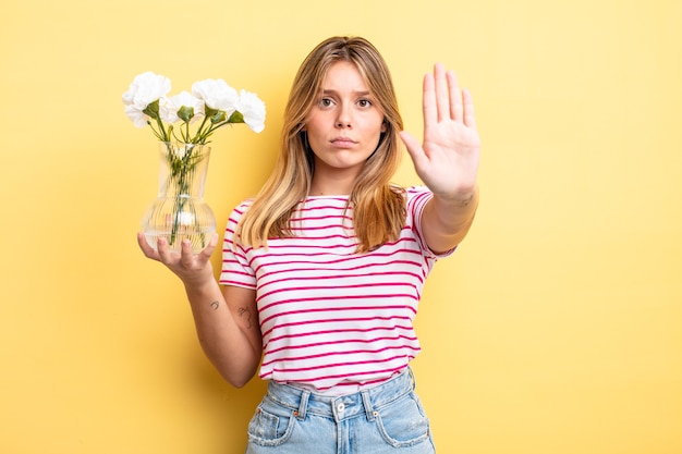 menina bonita loira olhando sério mostrando a palma da mão aberta, fazendo gesto de parada. conceito de flores decorativas