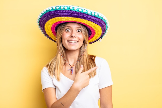 Menina bonita loira parecendo animada e surpresa, apontando para o lado. conceito de chapéu mexicano