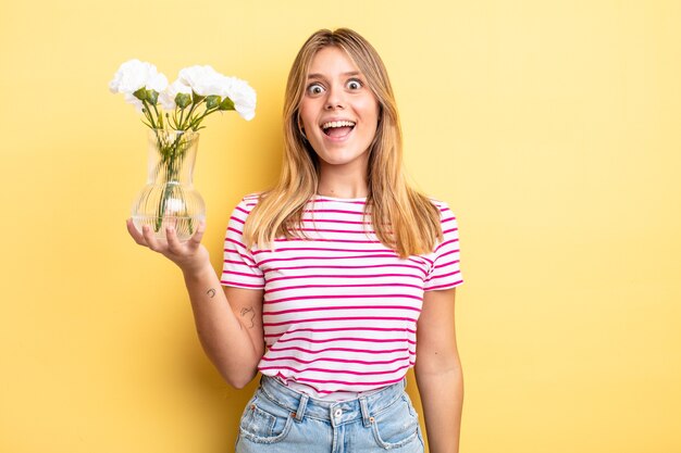 Menina bonita loira parecendo feliz e agradavelmente surpresa. conceito de flores decorativas