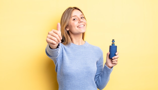 Menina bonita loira se sentindo orgulhosa, sorrindo positivamente com o polegar para cima. conceito de vaporizador de fumaça