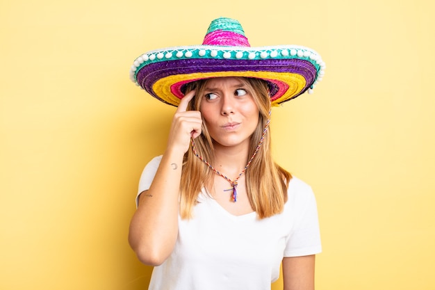 Menina bonita loira sorrindo alegremente e sonhando acordada ou duvidando. conceito de chapéu mexicano
