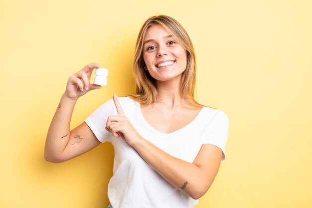 menina bonita loira sorrindo alegremente, sentindo-se feliz e apontando para o lado. conceito de frasco de comprimidos