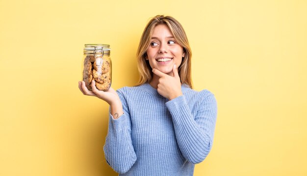 Menina bonita loira sorrindo com uma expressão feliz e confiante com a mão no queixo. conceito de biscoitos caseiros