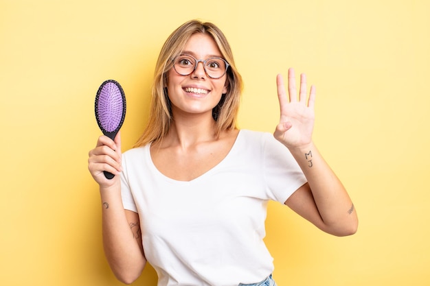 Menina bonita loira sorrindo e parecendo amigável, mostrando o número quatro. conceito de escova de cabelo