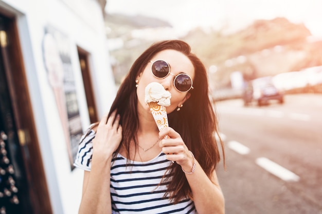 Menina bonita morena comendo sorvete e andar ao ar livre na rua.