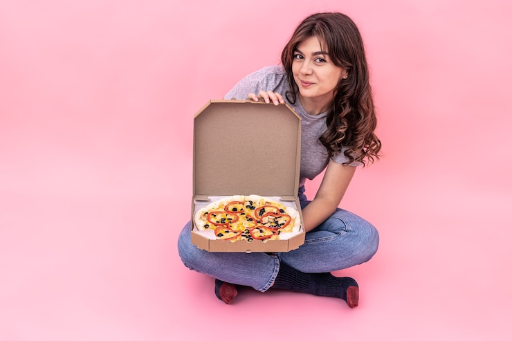Foto menina bonita morena sorridente se alegra com pizza da caixa de entrega, fundo rosa.