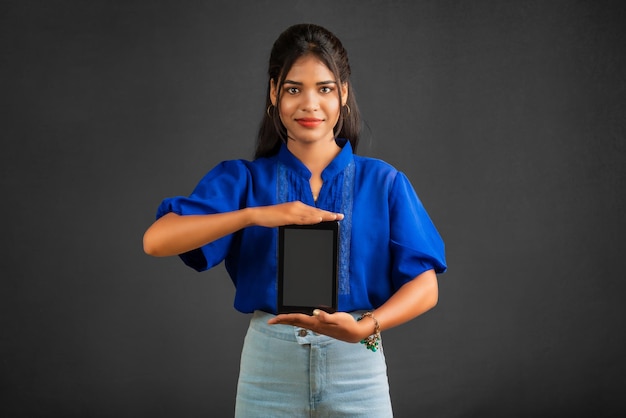 Menina bonita mostrando uma tela em branco de um smartphone ou celular ou tablet em um fundo cinza