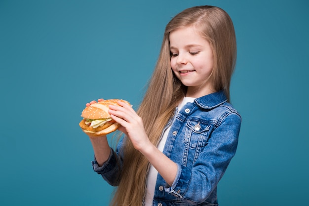 Menina bonita na jaqueta jeans com longos cabelos castanhos segurar um hambúrguer