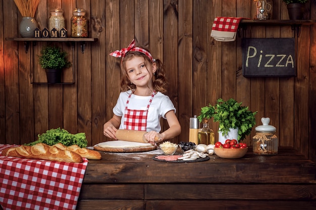 Menina bonita no avental xadrez, desenrolando a massa para pizza