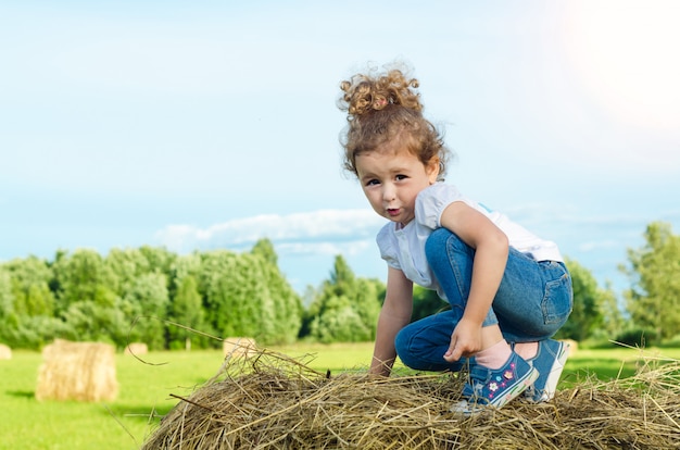 Menina bonita no campo, no palheiro de rolo. criança brinca durante a fenação. infância. colheita.