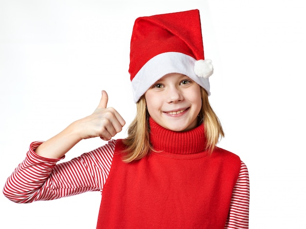 Menina bonita no chapéu de Papai Noel com polegares para cima o sinal está bem isolado