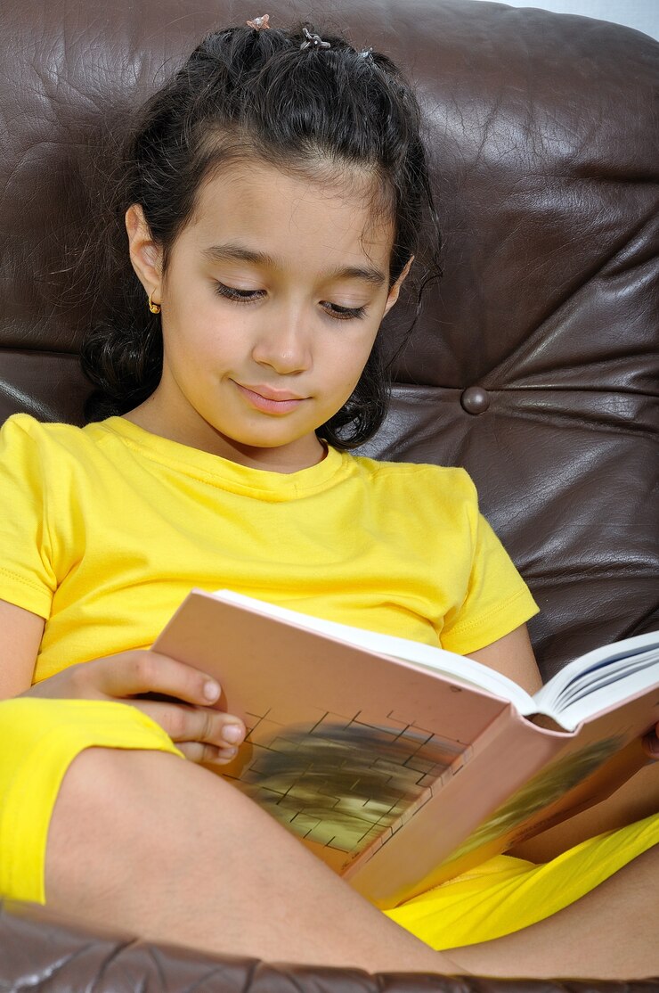 Foto menina bonita no livro de leitura amarelo no sofá